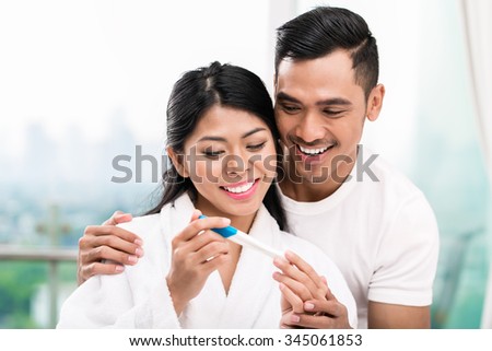 Asian woman surprising her husband with positive pregnancy test, he seems reasonably pleased