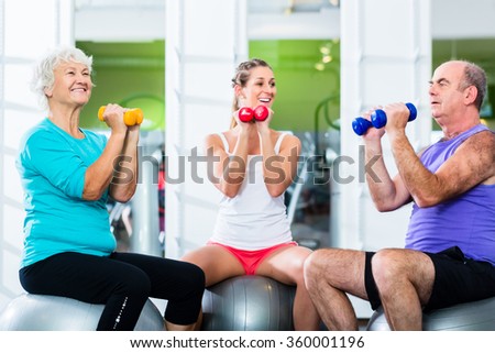 Senior man and women with fitness trainer in gym lifting barbells as sport exercise
