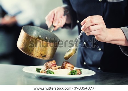 Chef pouring sauce on dish in restaurant kitchen, crop on hands, filtered image