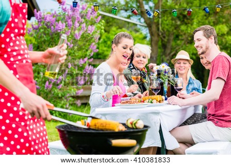 Man grilling meat and vegetables on garden party, his friends eating the bbq meat