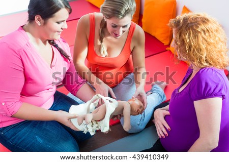 Midwife explaining birth process to pregnant women during antenatal class with anatomic model of pelvic bone
