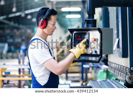Asian worker operating CNC metal skip in factory on the machine floor