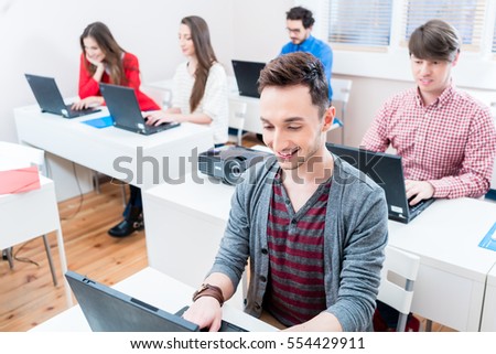 Student working on laptop PC in college, more women and men in background