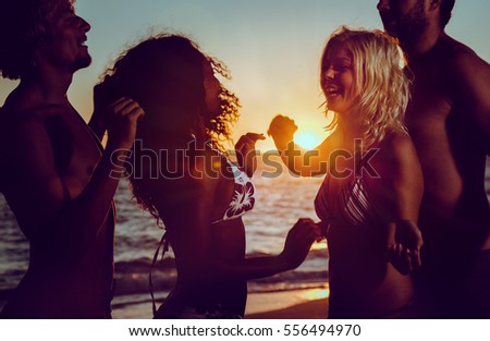 Men and women having party at ocean beach dancing in the sunset