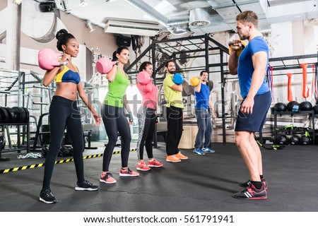 Men and women with coach at kettlebell functional training in fitness center