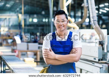 Worker in his carpenter workshop standing proud in front of the machines of the factory floor
