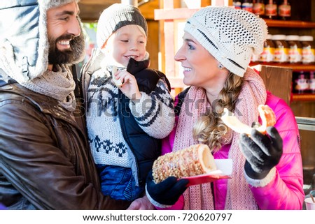 Family eating rolls and sausage on Christmas Market in front of tree