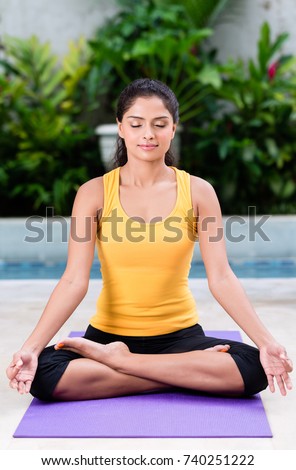 Serene young woman sitting in lotus position while practicing Hindu yoga outdoors