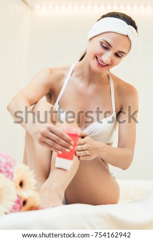 Fit young woman waxing her legs with a portable roll-on depilatory wax heater for painless hair removal at home