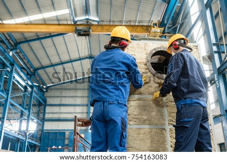 Two Asian workers applying insulation material to an industrial steam boiler