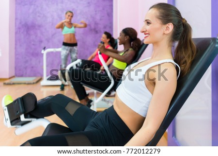 Side view of a beautiful woman smiling while exercising at the hip abductor machine during group workout at an exclusive fitness club for women