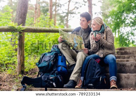 Hiking couple, woman and man, having break on a forest trail and reading the map