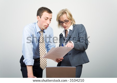 A man and a woman discussing a paper document in front of a notebook screen.