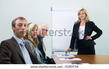 A group of people at a presentation held by a blond woman, looking at the viewer