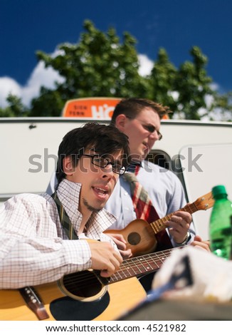 Two musicians making music in front of a trailer with a guitar and a ukulele
