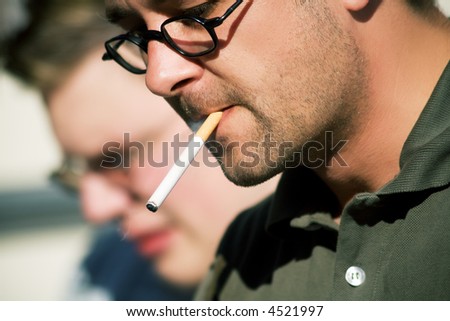 Man smoking a cigarette, in the background a second man is to be seen