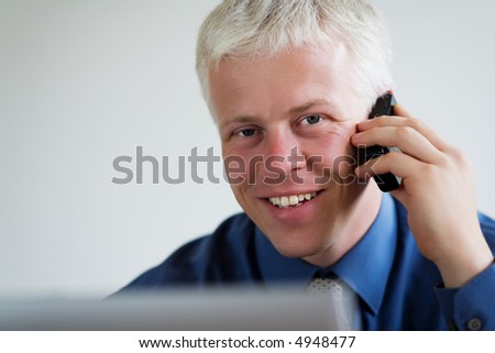 Portrait of a businessman on the phone, looking at the viewer over his laptop computer