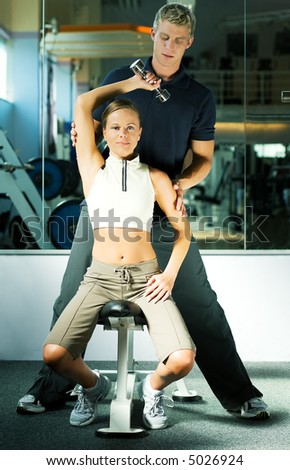 Woman lifting dumb-bells, the personal trainer helping her with the exercise