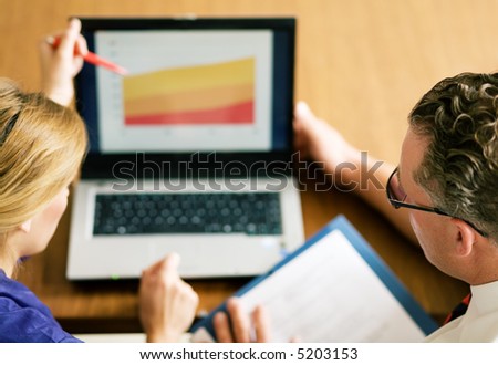 Two office workers (male / female) working on a presentation (very shallow depth of field, focus on glasses of the man)