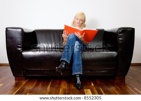 Woman sitting on a black sofa reading in a red book