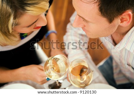 Young couple romantic dinner: clinking the white wine glasses; focus on the eyes of the people