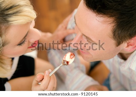 Young couple romantic dinner: she is feeding him with desert (yoghurt mousse); focus on faces