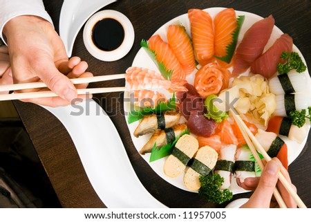 Two people (only hands to be seen) eating sushi; focus on the food