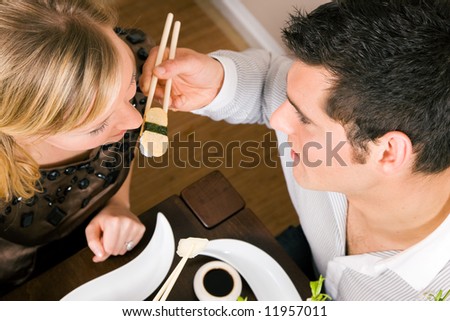 Couple feeding each other with sushi for dinner, romantic setting, presumably this is an advanced date; shallow focus on eyes