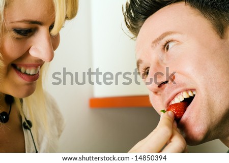 Couple in the kitchen: she is feeding him strawberries