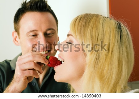 Couple in the kitchen: he  is feeding her strawberries