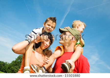 Family carrying their two sons on their shoulders under a perfect sky