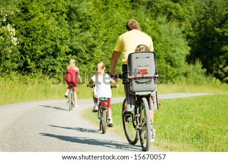 Family with two kids riding their bicycles on a summer day (seen from behind)