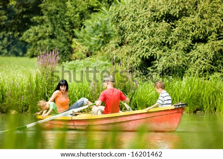 Family with two kids having a boat trip on a lake, in the background lots of trees and flowers