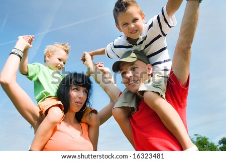 Family carrying their two kids piggyback under a perfect blue sky