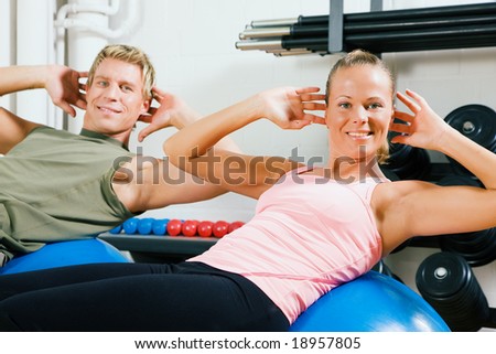 Couple doing situps on a fitness ball as training in the gym