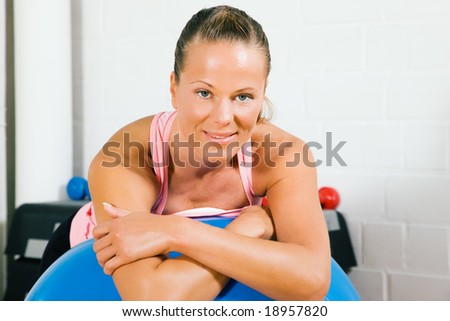 Woman leaning on top of a blue fitness ball having a break from her training looking at the viewer
