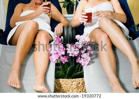 Two women (only torso to be seen) relaxing on beds in a health spa drinking juice