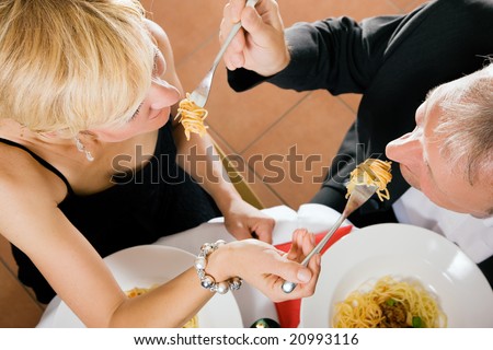 Romantic mature couple having dinner feeding each other with pasta in a fancy restaurant