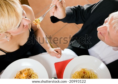 Romantic mature couple having dinner, he feeding her with delicious pasta