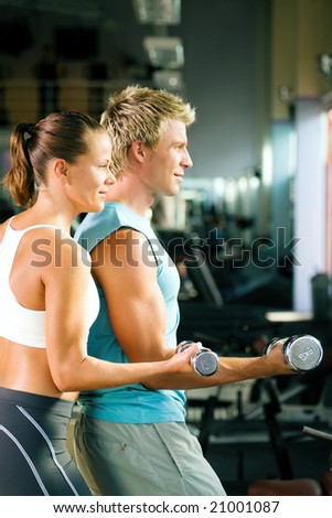 Fitness couple in the gym, rivaling each other, exercising with weights (focus on the face of the girl)
