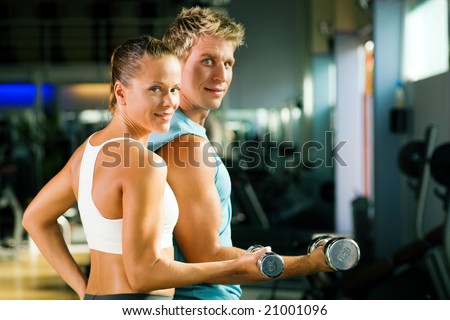 Fitness couple in the gym, rivaling each other, exercising with weights (focus on the face of the girl)