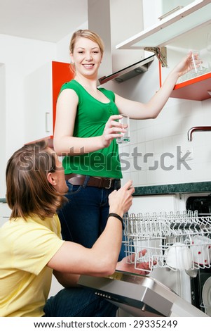 Couple emptying the dishwasher and sorting the dishes in a kitchen cupboard