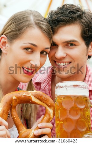 Couple in traditional German costume in a beer tent, he is having a drink, she a pretzel