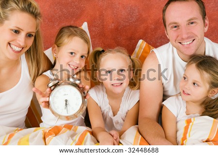 Family in bed in the morning, on child holding a clock â?? metaphor for getting up to enjoy the day