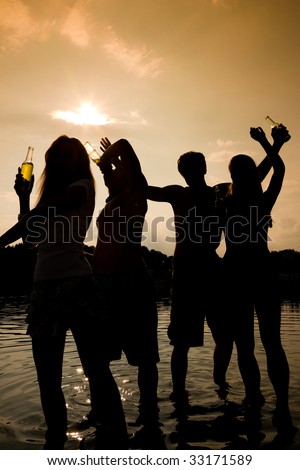 People (two couples) on the beach dancing to music, drinking and having a lot of fun in the sunset - only silhouette of people to be seen
