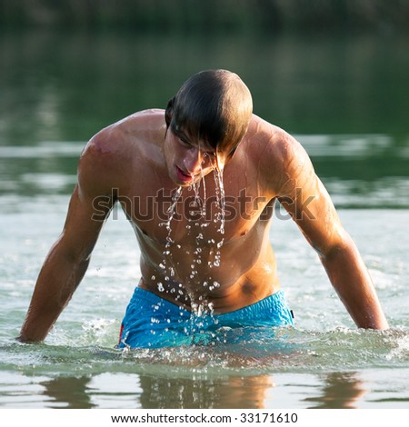 Very athletic swimmer getting out of the water, drops running down his body