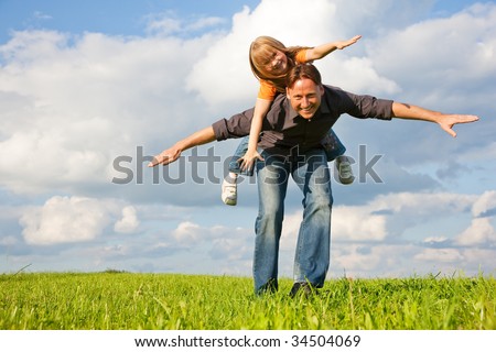 Father and his kid - daughter - playing together at a meadow, he is carrying her piggyback