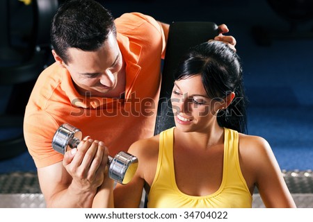 Woman with her personal fitness trainer in the gym exercising with dumbbells
