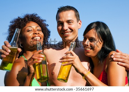 Group of friends - one man hugs two women and all have drinks in swimwear