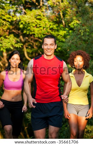 Group of friends exercising - man and two women jogging outdoors in beautiful evening light